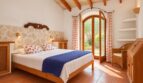 Helles Schlafzimmer der Natursteinfinca mit Holzbalkendecke, Doppelbett und Terrassentür zum Garten.