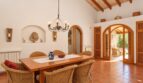 Heller Essbereich der Finca mit Holztisch, Korbstühlen, Gewölbetüren und rustikalem Holzbalkendecke.