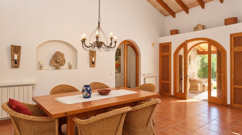 Heller Essbereich der Finca mit Holztisch, Korbstühlen, Gewölbetüren und rustikalem Holzbalkendecke.