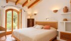 Helles Schlafzimmer der Natursteinfinca mit Holzbalkendecke, Terrakottaboden und Bogentür zum Garten.