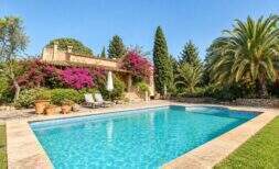 Natursteinfinca in Sa Pobla mit blauem Pool, Bougainvillea-Fassade, Palmen und Sonnenliegen im Garten.
