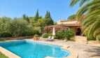 Natursteinfinca mit türkisblauem Pool, Liegestühlen und blühender Bougainvillea im gepflegten Garten.