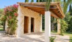 Außenansicht der Natursteinfinca mit Holzdach-Pergola, Bougainvillea und gepflegtem Garten.
