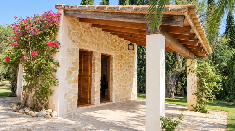 Außenansicht der Natursteinfinca mit Holzdach-Pergola, Bougainvillea und gepflegtem Garten.