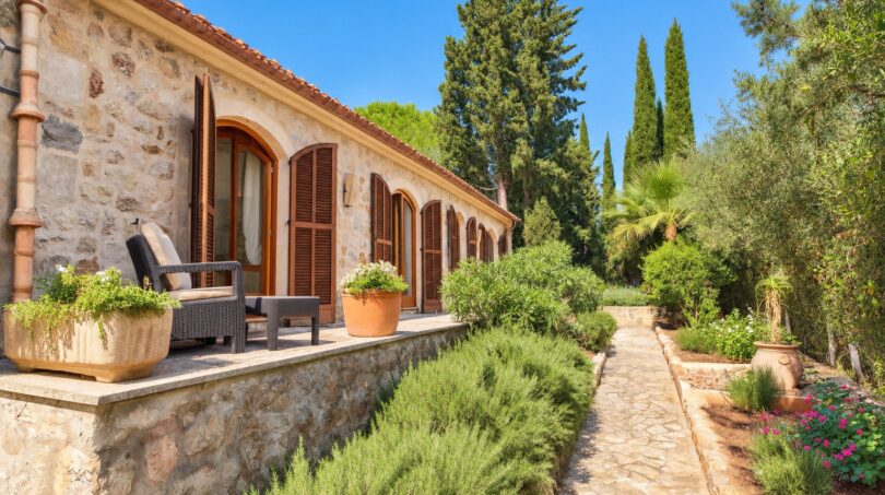 Mediterrane Natursteinfinca mit Holzläden, Terrasse und gepflegtem Garten mit Lavendel und Zypressen.