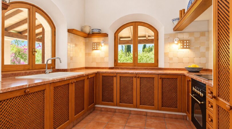 Mediterrane Landhausküche mit Holzschränken, Bogenfenstern und Terrakottaboden in authentischer Natursteinfinca.