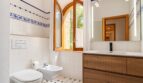 Helles Badezimmer der Finca mit Bogenfenster, Holzwaschtisch, Bidet und blau-weißen Fliesen.