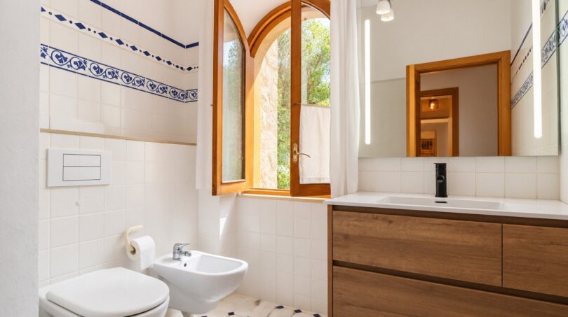 Helles Badezimmer der Finca mit Bogenfenster, Holzwaschtisch, Bidet und blau-weißen Fliesen.
