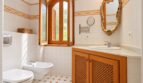 Elegantes Finca-Bad mit Holzschränken, Goldrahmenspiegel, Bidet und dekorativem Fliesenmuster in Weiß-Orange.
