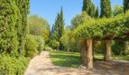Gepflegter Gartenweg der Natursteinfinca mit Pergola, Zypressen und grüner Rasenfläche.
