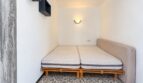 Kleines Schlafzimmer mit zwei Einzelbetten auf Holzgestell, Wandlampe und Wandregal in Strandwohnung Palma