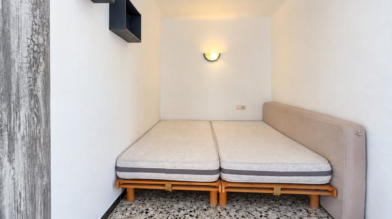 Kleines Schlafzimmer mit zwei Einzelbetten auf Holzgestell, Wandlampe und Wandregal in Strandwohnung Palma