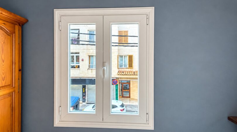 Weißes Doppelflügelfenster in grauem Zimmer mit Blick auf Stadtstraße in Playa de Palma, Mallorca