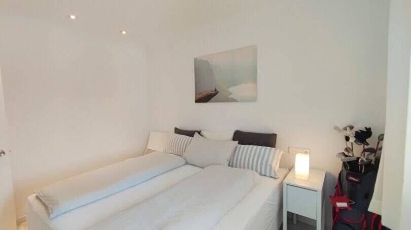 Helles Schlafzimmer mit Doppelbett, Nachttischlampe und Golfbag in der Ferienwohnung über der Bucht von Cala Mandia