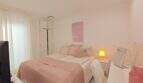 Helles Schlafzimmer mit Doppelbett in Rosa, weißen Einbauschränken und Schreibtisch in der Ferienwohnung Cala Mandia