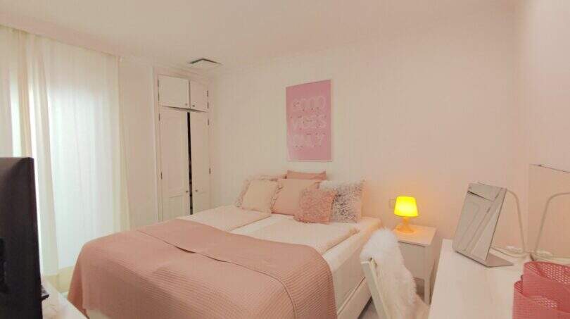 Helles Schlafzimmer mit Doppelbett in Rosa, weißen Einbauschränken und Schreibtisch in der Ferienwohnung Cala Mandia