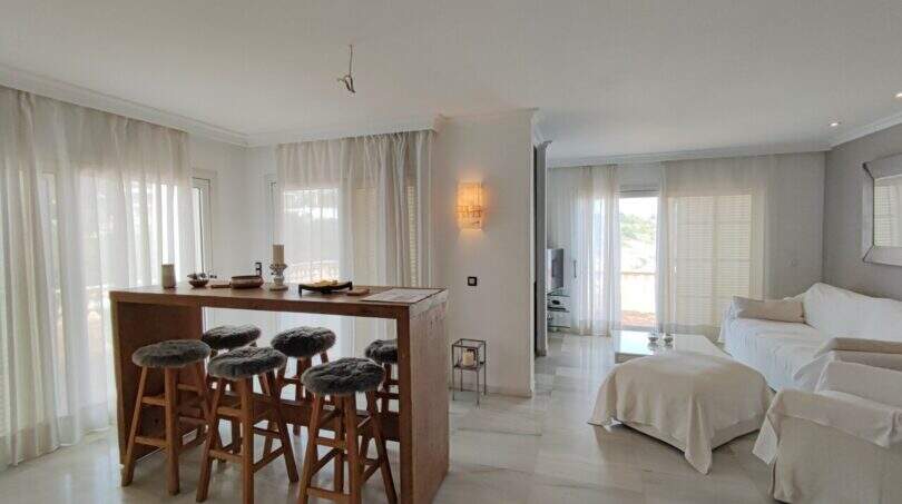 Helles Wohnzimmer mit Holz-Bartheke, flauschigen Barhockern und weißen Sofas in Villa über Cala Mandia