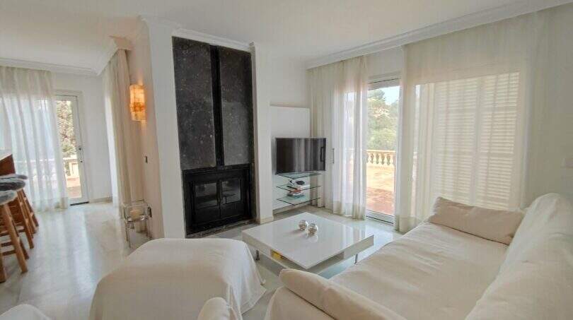 Helles Wohnzimmer mit weißen Sofas, Kamin und Terrassenzugang in der Villa über der Bucht von Cala Mandia