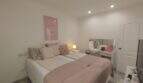 Helles Schlafzimmer mit rosa Doppelbett, Spiegel und Einbaustrahler in der Ferienwohnung Cala Mandia