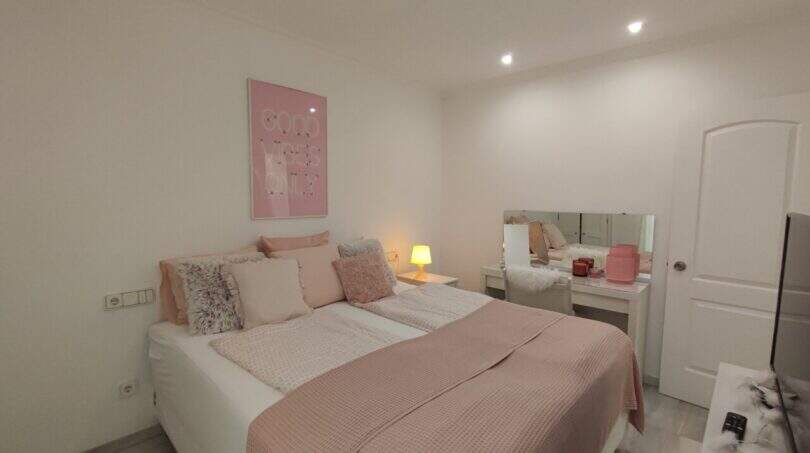 Helles Schlafzimmer mit rosa Doppelbett, Spiegel und Einbaustrahler in der Ferienwohnung Cala Mandia