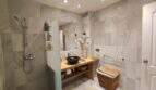 Modernes Badezimmer der Ferienwohnung in Cala Mandia mit Regendusche, Holzwaschtisch und eleganten Marmorfliesen.