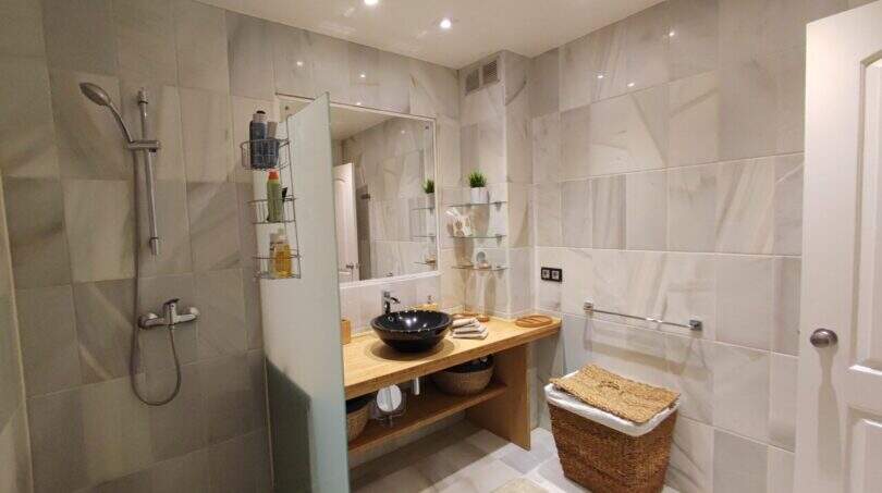 Modernes Badezimmer der Ferienwohnung in Cala Mandia mit Regendusche, Holzwaschtisch und eleganten Marmorfliesen.