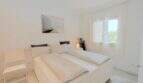 Helles Schlafzimmer mit Doppelbett, weißer Einrichtung und Fenster mit Grünblick in der Villa Cala Mandia