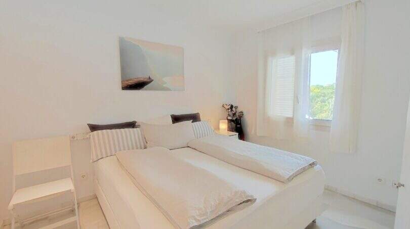 Helles Schlafzimmer mit Doppelbett, weißer Einrichtung und Fenster mit Grünblick in der Villa Cala Mandia
