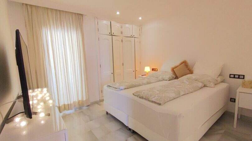 Helles Schlafzimmer mit Doppelbett, weißem Einbauschrank und TV in der Ferienwohnung über der Bucht von Cala Mandia