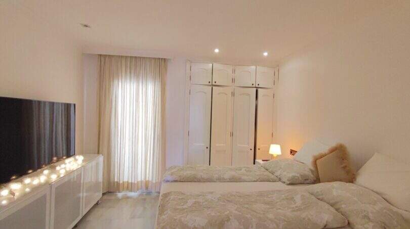 Helles Schlafzimmer mit Doppelbetten, weißem Einbauschrank, TV und dekorativer Lichterkette in Cala Mandia
