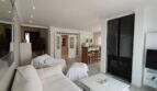 Helles Wohnzimmer mit weißen Sofas, modernem Kamin und offenem Küchenbereich in der Villa über der Bucht von Cala Mandia.
