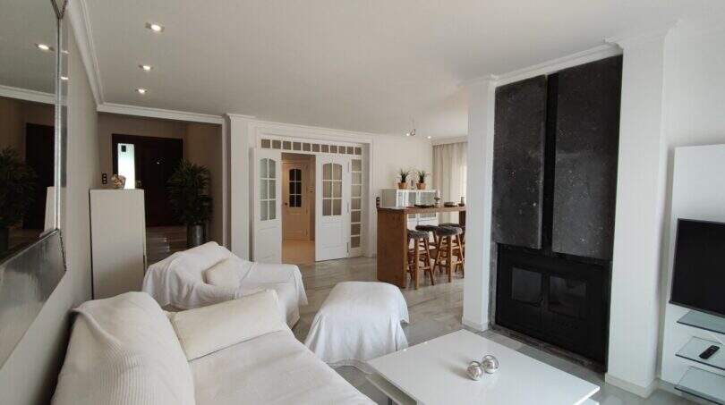 Helles Wohnzimmer mit weißen Sofas, modernem Kamin und offenem Küchenbereich in der Villa über der Bucht von Cala Mandia.