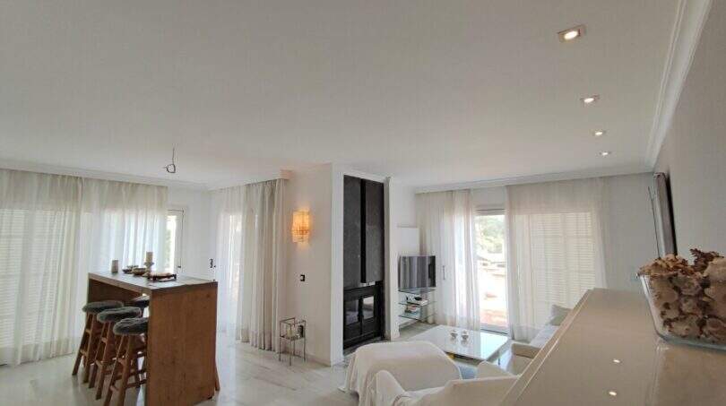 Helles Wohnzimmer mit Kamin, offener Küche, weißen Möbeln und großen Fenstern in Villa bei Cala Mandia