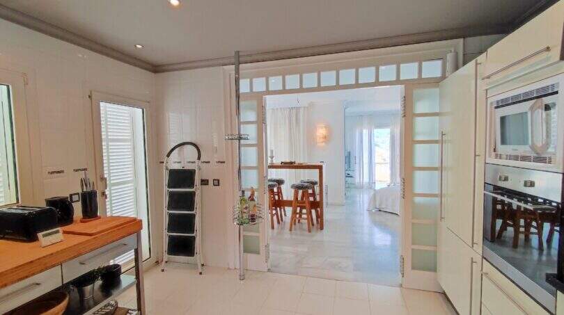 Moderne Küche mit Glasschiebetür zum Essbereich, weißen Einbaugeräten und Holzarbeitsfläche in der Villa Cala Mandia
