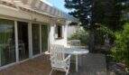 Sonnige Terrasse mit weißen Gartenmöbeln, Markise und Glasschiebetür beim Chalet in Portocolom