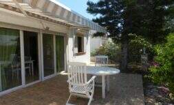 Sonnige Terrasse mit weißen Gartenmöbeln, Markise und Glasschiebetür beim Chalet in Portocolom