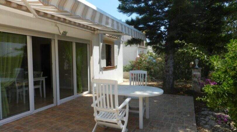 Sonnige Terrasse mit weißen Gartenmöbeln, Markise und Glasschiebetür beim Chalet in Portocolom