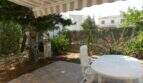 Überdachte Terrasse mit Markise, weißen Gartenmöbeln und gepflegtem Garten beim Chalet in Portocolom.
