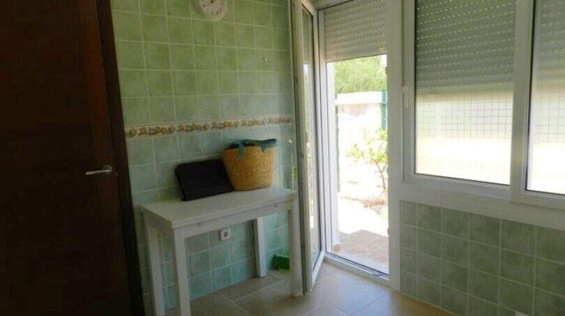 Heller Hauswirtschaftsraum mit grünen Wandfliesen, weißem Tisch, Wanduhr und Tür zum Außenbereich in Chalet Portocolom