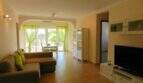 Helles Wohnzimmer mit Ecksofa, TV, grünen Vorhängen und Terrassenzugang im Chalet Portocolom