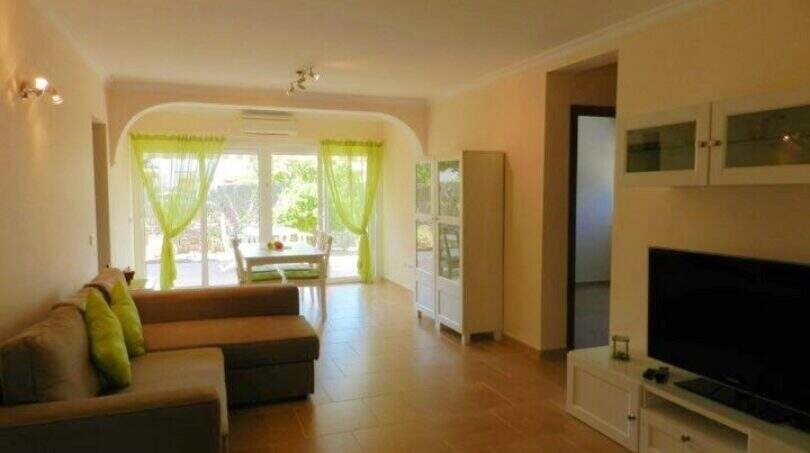 Helles Wohnzimmer mit Ecksofa, TV, grünen Vorhängen und Terrassenzugang im Chalet Portocolom